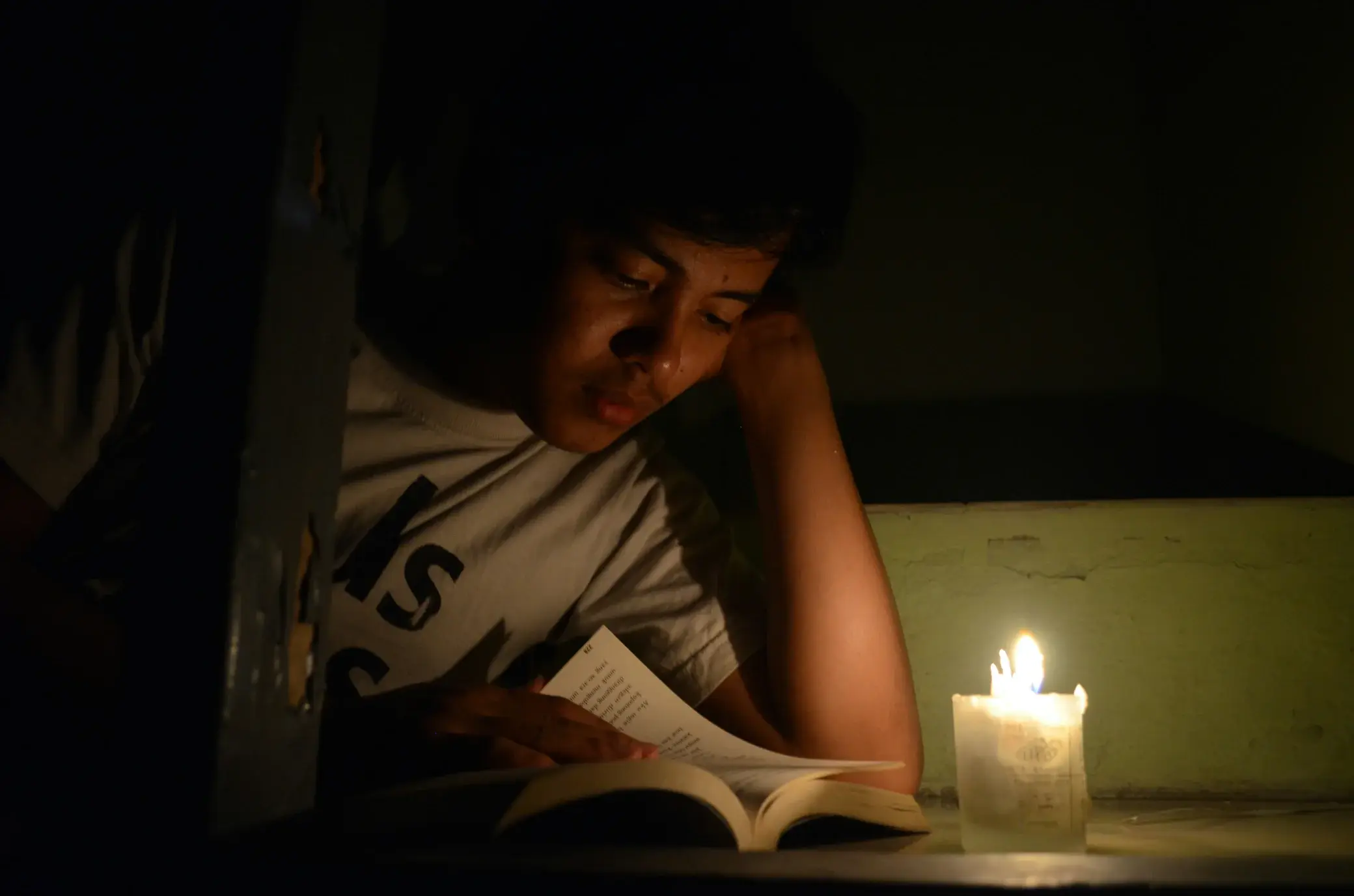 Person reading a book by candlelight on a winter evening with standby generator installation for safety